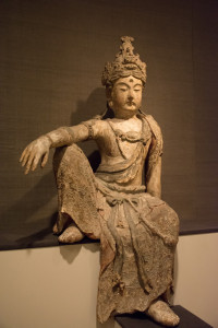 A sculpture of the Chinese Buddhist deity Guanyin. He is seated with his right knee pushed upward while resting his right arm upon it.
